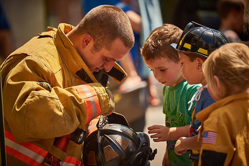 Firefighter showing his helmet to three young children
