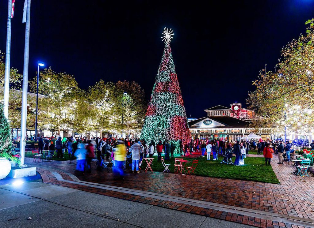 Easton Town Square lighted for holiday with giant Christmas Tree in center of gathered crowd at night.