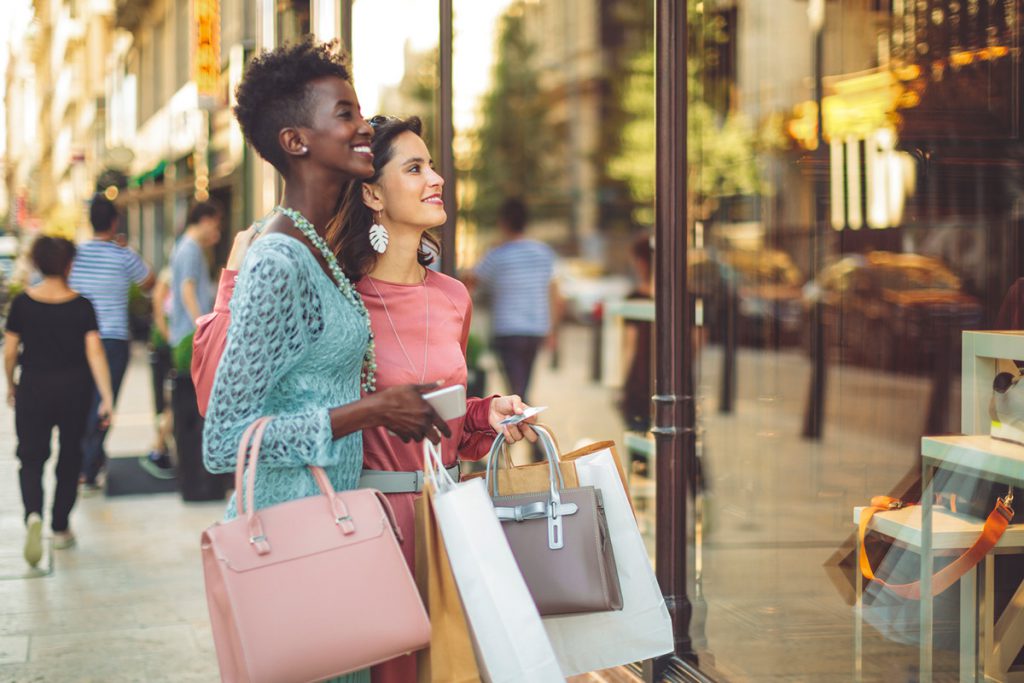 Two women with shopping bags window-shopping on a metropolitan street.